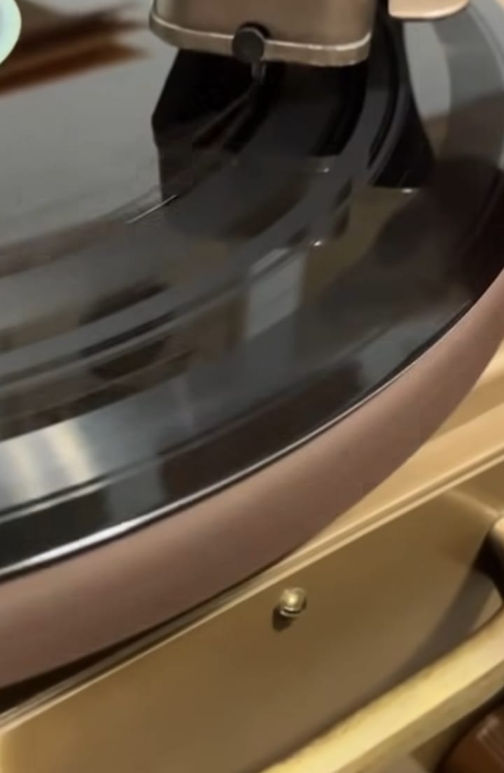 Cutting head resting on a spinning black disc on a gold and brown Hoffman record cutter.