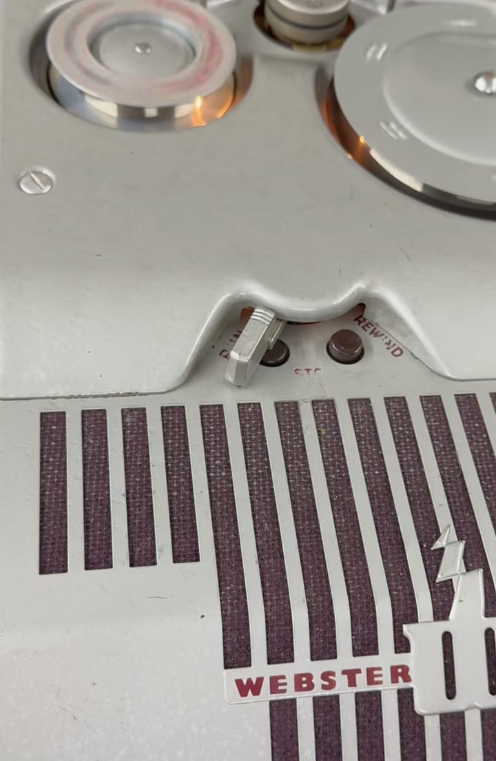 Top deck of a gray Webster-Chicago wire recorder: two spools, the run/stop/rewind lever, and a maroon speaker grille.